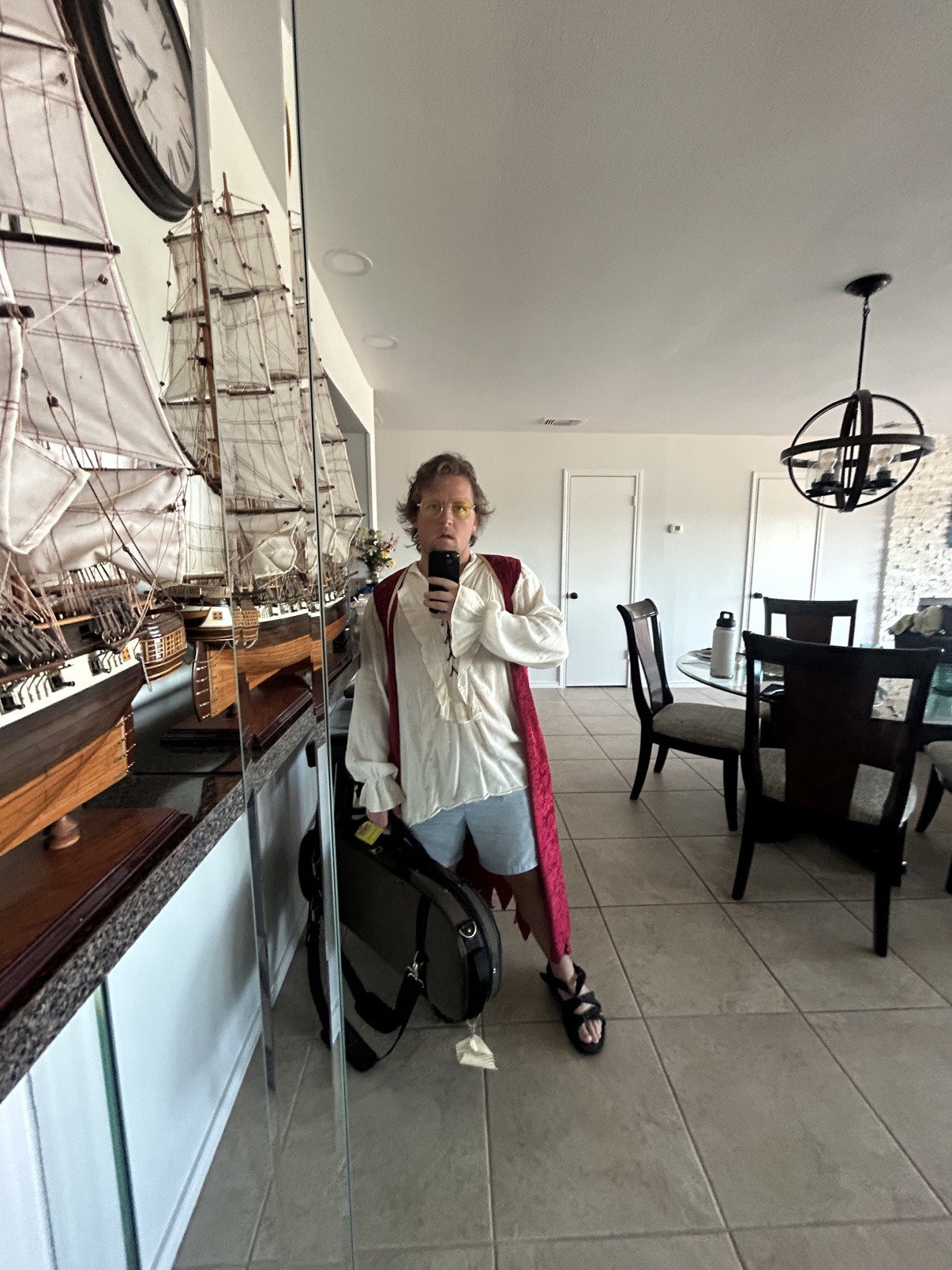 Fiddle in pirate costume holding his violin case beside model ships