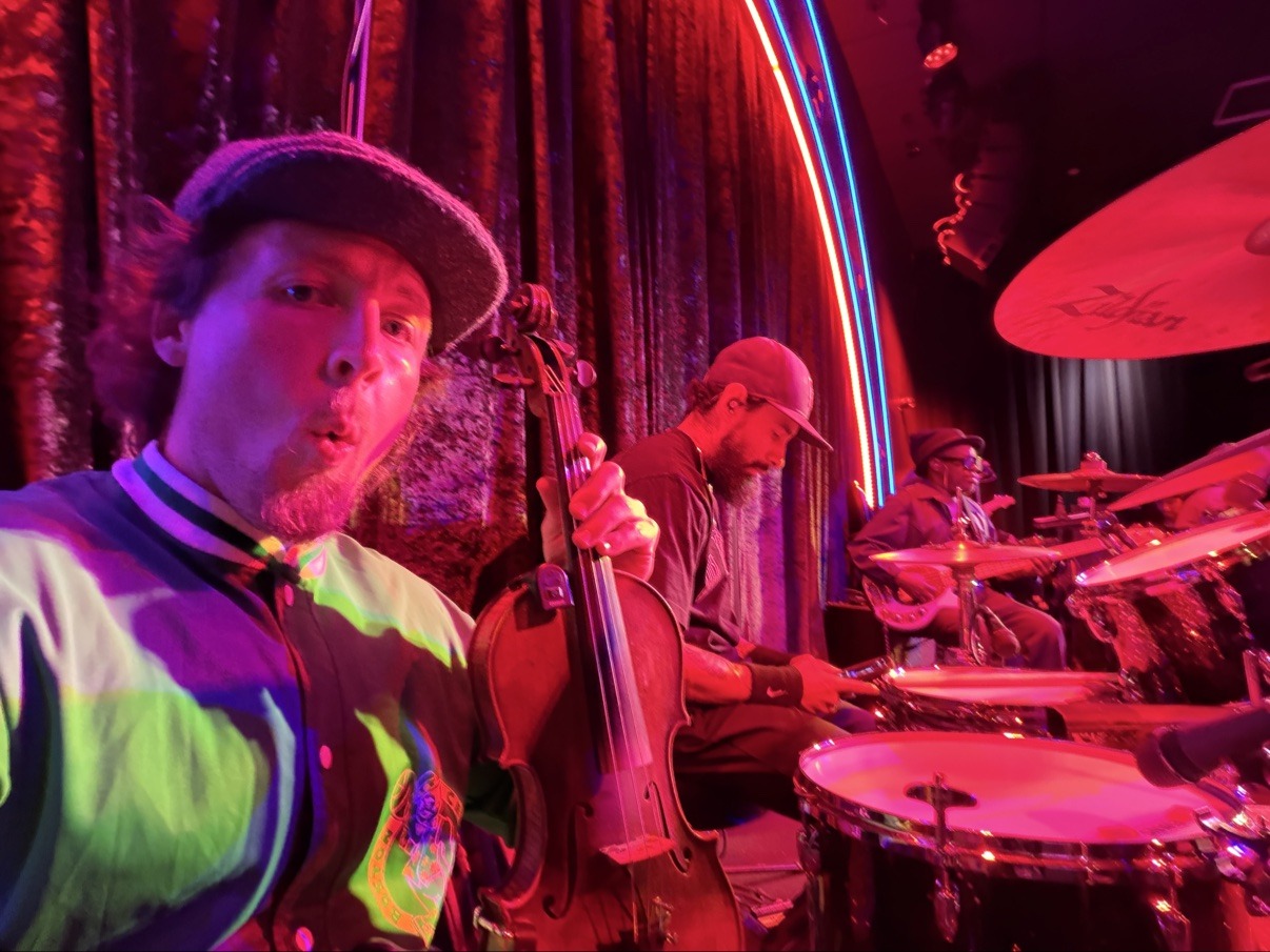 Jake holding his violin beside a red-lit stage