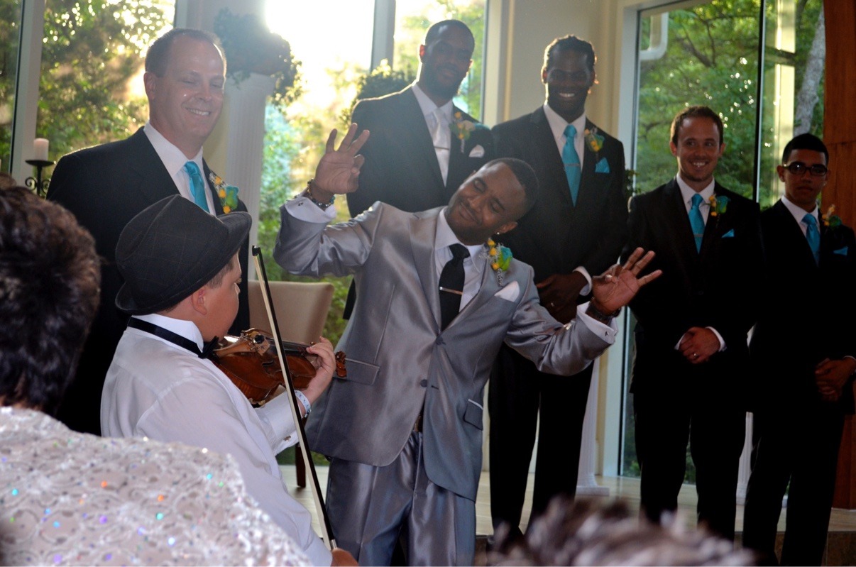 A young Jake playing violin during a wedding ceremony with the wedding party