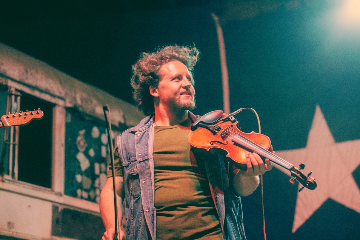 Jake performing onstage in a denim vest in front of a star-spangled backdrop