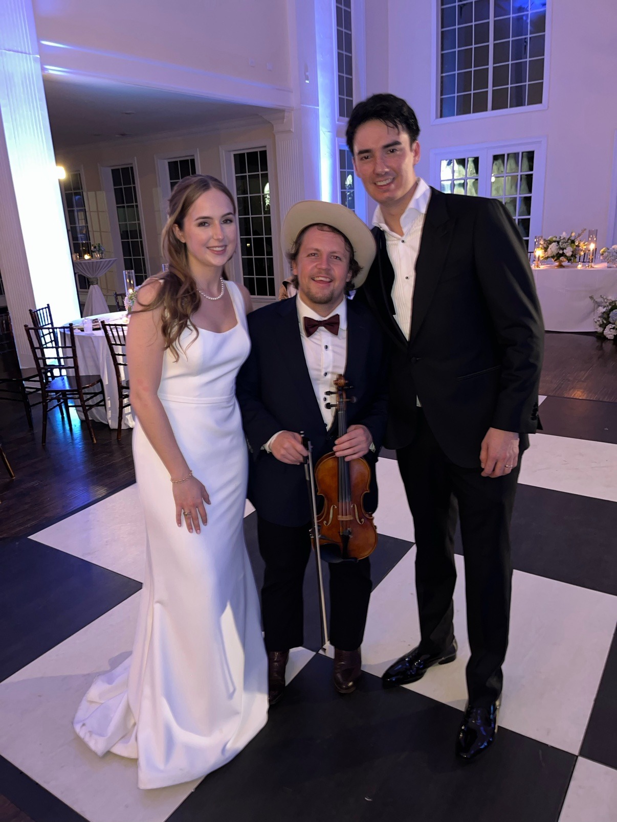 Jake holding his violin beside a newly married couple