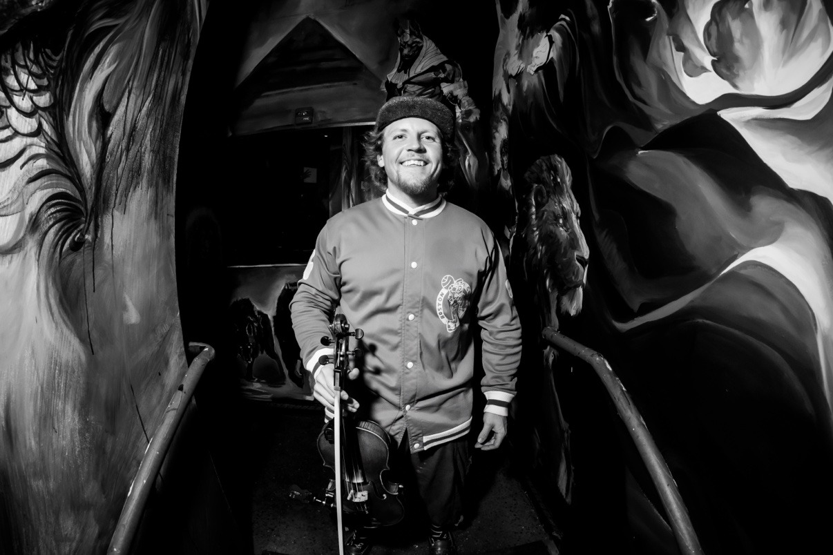 Jake Kennedy holding his violin in a mural-covered hallway backstage