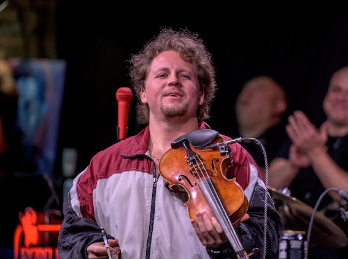 Jake Kennedy holding his violin on stage at Kill Tony